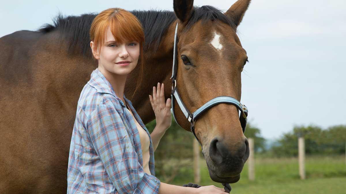 A woman stroking a horse in a field.