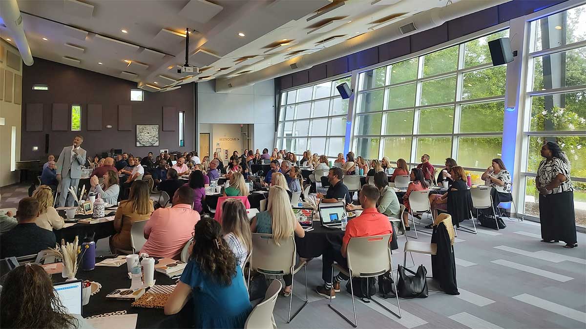 Engaged audience at the Hernando Schools Leadership Conference Event listening intently to a speaker at the front of a modern meeting room.